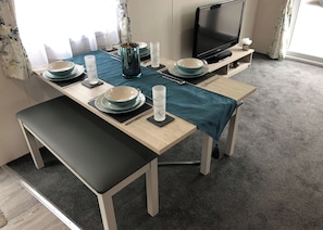 Un coin repas avec une table dressée pour quatre personnes, un téléviseur et une fenêtre avec des rideaux.