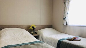 Habitación de hotel con dos camas, una mesita de noche, un florero con flores y una ventana con cortinas.