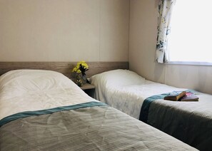 Une chambre d’hôtel avec deux lits, une table de chevet, un vase avec des fleurs et une fenêtre avec des rideaux.