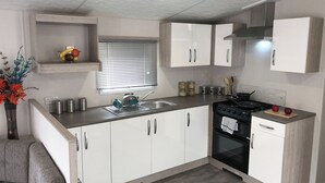Una cocina moderna con armarios blancos, un lavamanos de acero inoxidable, una estufa y una ventana con persianas.