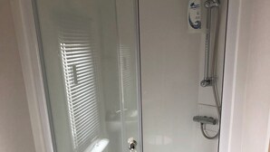 Un baño con cabina de ducha de vidrio, cabezal de ducha de mano y una botella de champú.