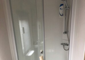 Une salle de bain avec une douche à parois de verre, un pommeau de douche amovible et une bouteille de shampoing.