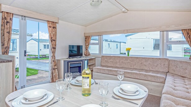 A dining area with a table set for four, a television, and a sofa. - Caravan with one double and two twin. (Prestatyn, Denbighshire)