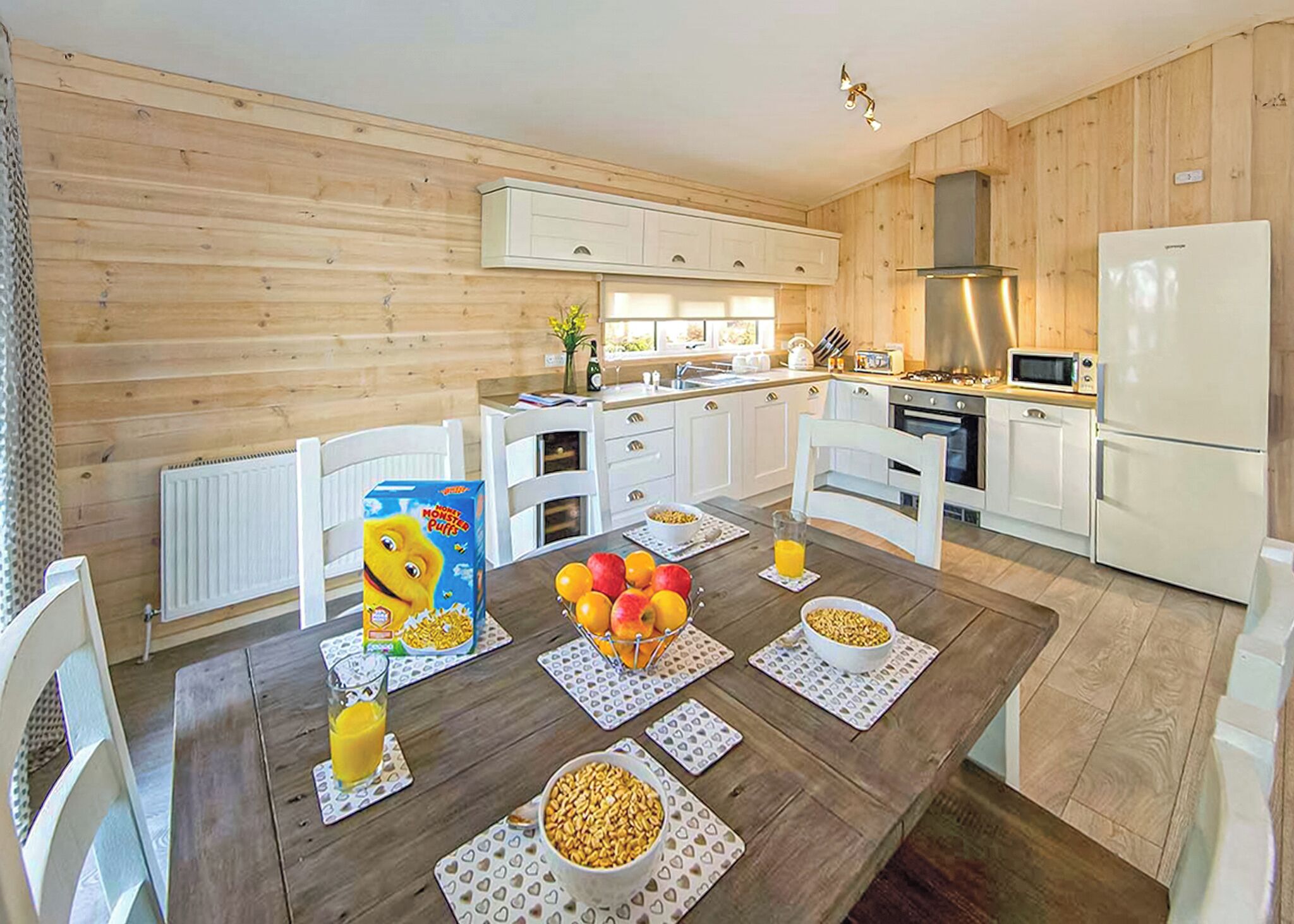 A modern kitchen with white cabinets, a wooden dining table with placemats, and a breakfast setting.