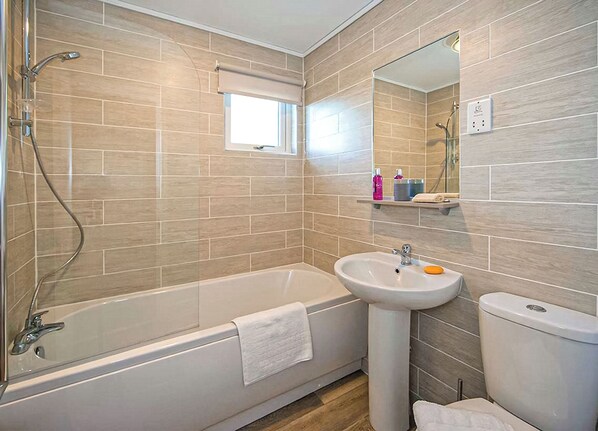Ein Badezimmer mit Badewanne, Waschbecken und Toilette, mit gefliesten Wänden und einem Fenster.