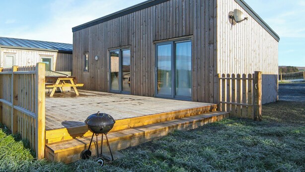 A wooden building with a deck, a barbecue grill, and a fenced area.