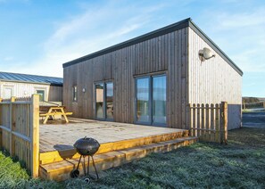 Een houten gebouw met een terras, een barbecue en een omheind gebied.