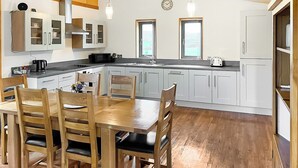 A modern kitchen with wooden cabinets, a dining table with chairs, and two windows.