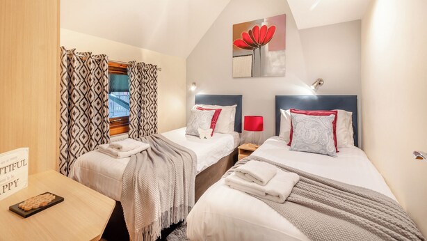 A bedroom with two beds, a wooden desk, a sign, and a window with curtains.