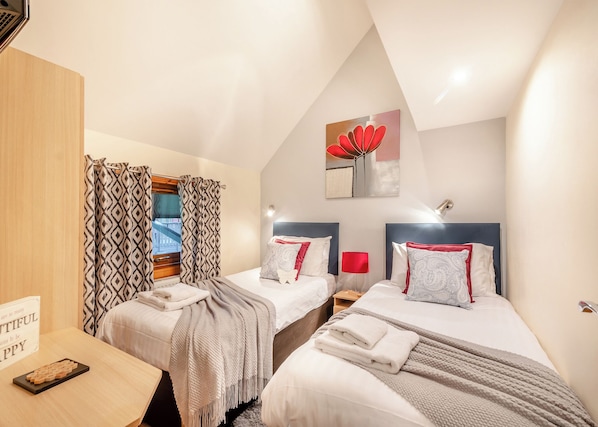 A bedroom with two beds, a wooden desk, a sign, and a window with curtains.