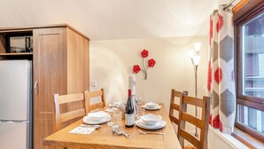 A dining area with a wooden table set for four, a bottle of wine, and a decorative wall with red flowers.