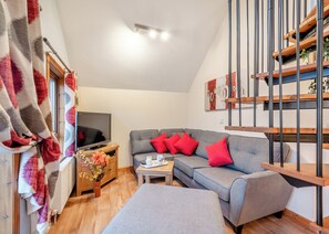 A modern living room with a grey sofa, red cushions, a flat-screen TV, a wooden side table, and a staircase with metal railings.
