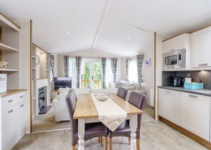 A modern, well-lit room with a dining table, chairs, a sofa, a television, and a kitchen area with a microwave. - 2 bedroom accommodation in Calthwaite, Nr Penrith (Calthwaite, Nr Penrith)
