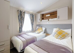 Un dormitorio con dos camas, una ventana con cortinas, un estante de madera sobre las camas y un armario.