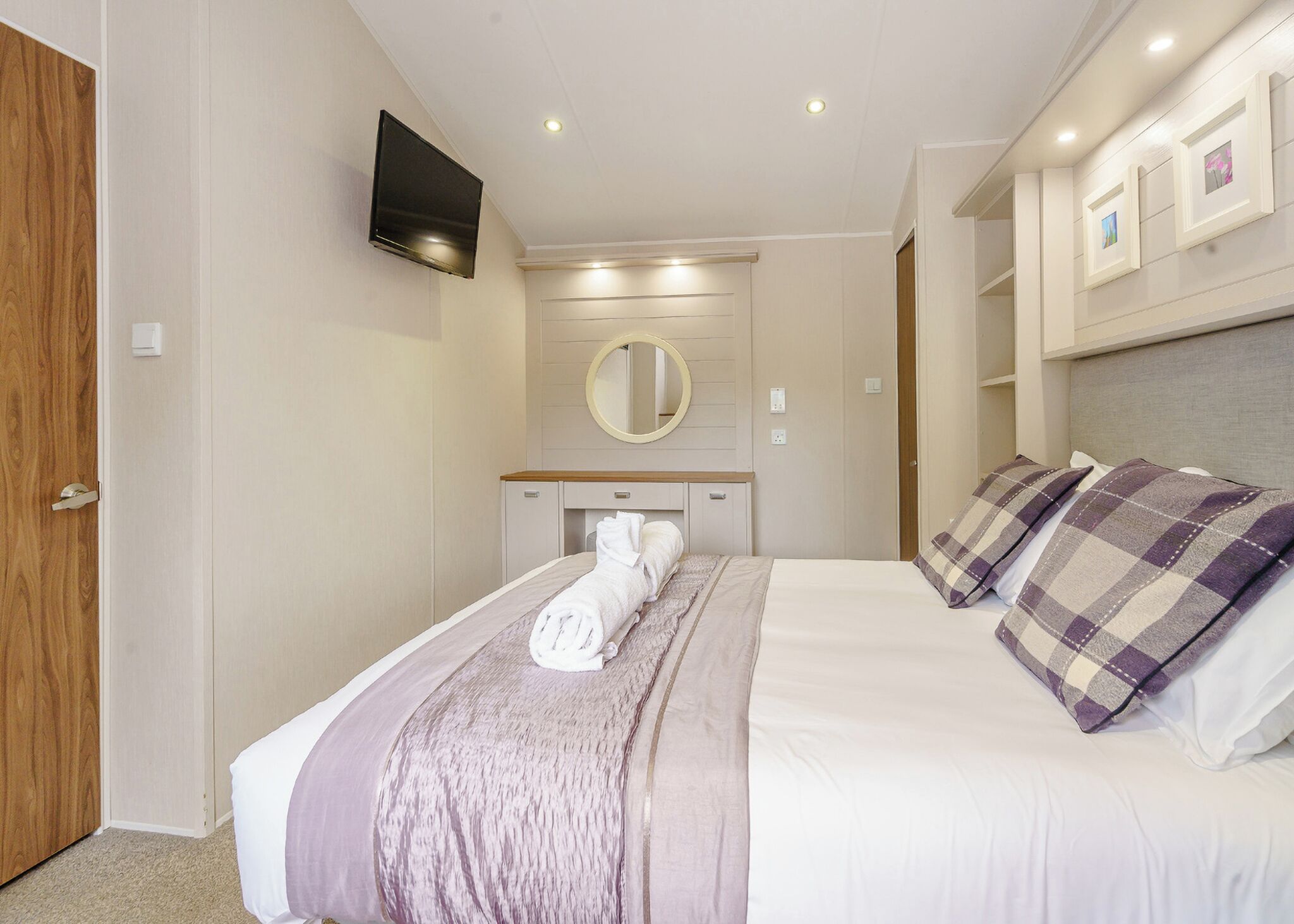 A bedroom with a bed, a TV, a mirror, and a door.