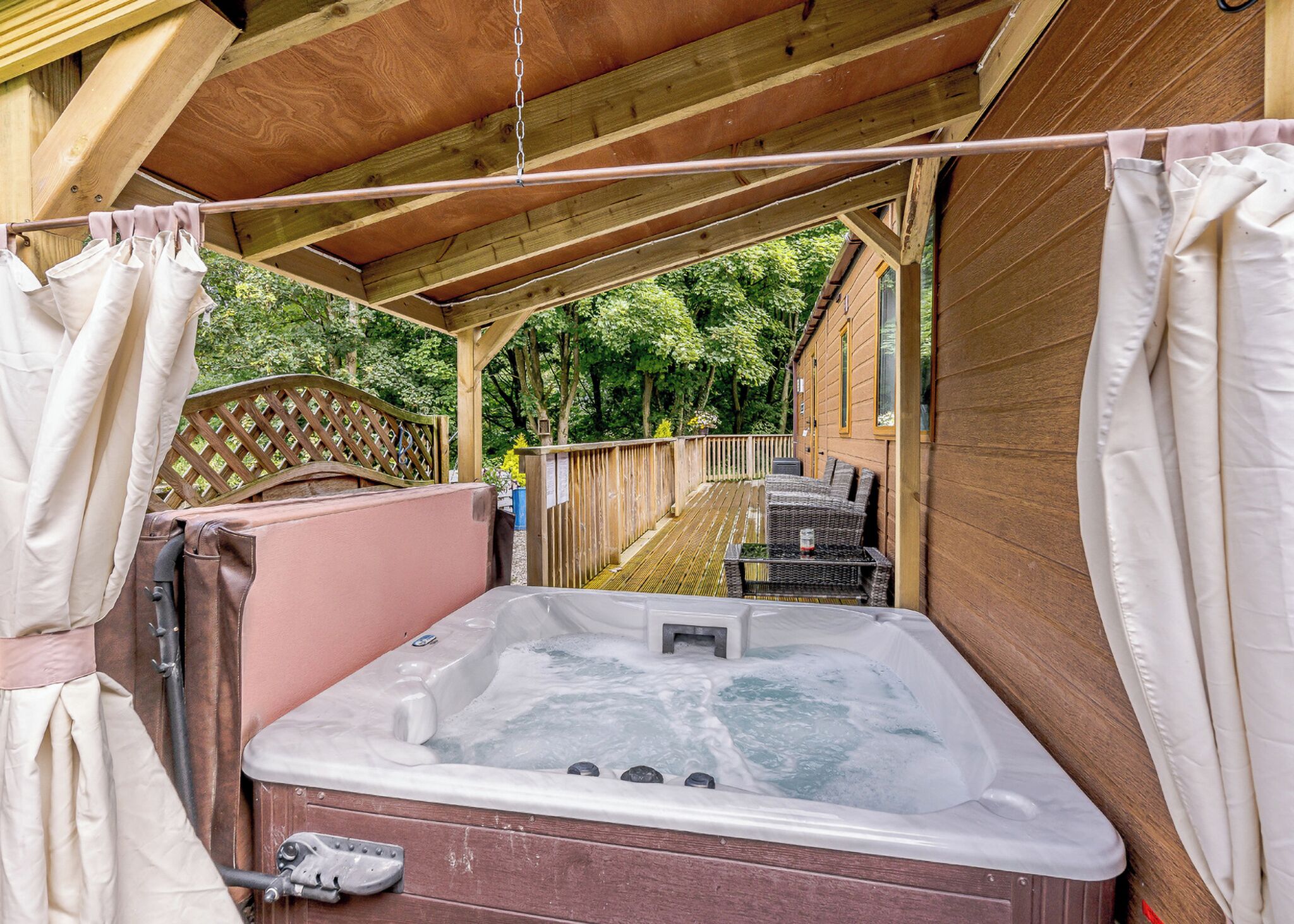A hot tub in an outdoor wooden deck area with a wooden fence and greenery in the background.