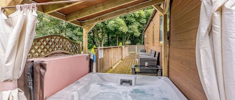 Un jacuzzi en un área de terraza de madera al aire libre, con un cerramiento de madera y follaje en el fondo.