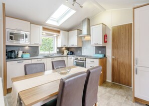 A compact kitchen with a skylight, a stove, a microwave, and a dining area with chairs. - 2 bedroom accommodation in Calthwaite, Nr Penrith (Calthwaite, Nr Penrith)