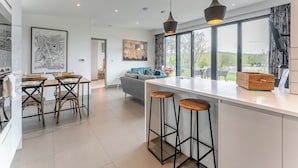 A modern kitchen with a central island, bar stools, a dining area with chairs, and a large window with a view. - 2 bedroom accommodation in Lewes (Lewes)