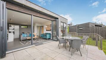 A modern house with a patio, a dining area, and a living room with a sofa and a TV.