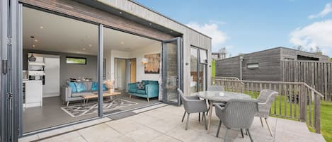 A modern house with a patio, a dining area, and a living room with a sofa and a TV.