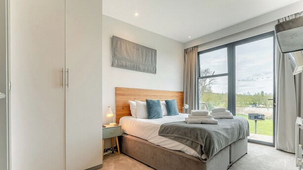 A modern bedroom with a large bed, a nightstand, a wardrobe, and a view of the outdoors. - 2 bedroom accommodation in Lewes (Lewes)
