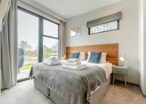 Una moderna camera d'albergo con un letto grande, una testiera in legno, un comodino con una lampada e vista sull'esterno.