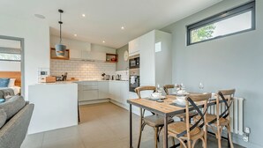 A modern kitchen with white cabinets, a dining area with wooden chairs, and a large window. - 2 bedroom accommodation in Lewes (Lewes)