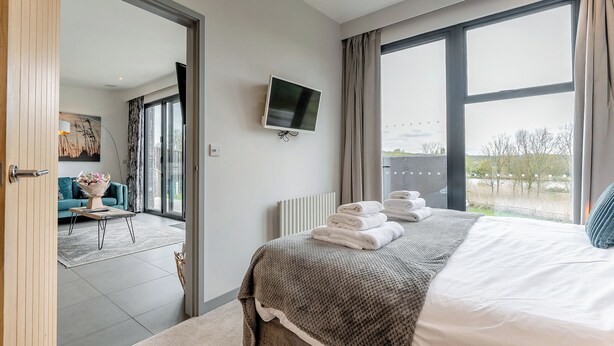 A modern hotel room with a large bed, a flat-screen TV, and a view of the outdoors.