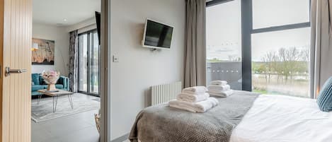 A modern hotel room with a large bed, a flat-screen TV, and a view of the outdoors.