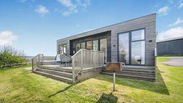 A modern house with a deck, large windows, and a grill.