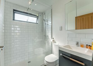 A modern bathroom with white subway tiles, a glass-enclosed shower, a toilet, a sink with toiletries, and a wooden vanity. - 2 bedroom accommodation in Lewes (Lewes)