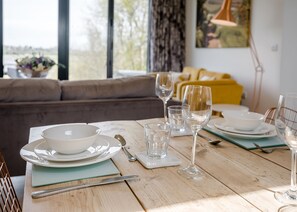 A dining table set with plates, bowls, cutlery, and glasses, with a sofa and yellow cushions in the background. - 2 bedroom accommodation in Lewes (Lewes)