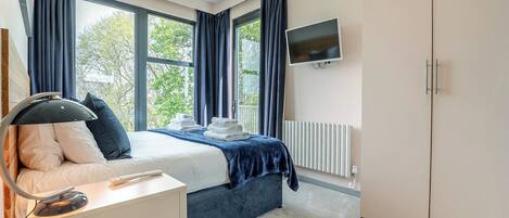 A bedroom with a bed, bedside table, TV, and a radiator.