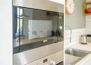 A kitchen with a built-in microwave oven, a stainless steel sink, and a wall-mounted clock. - 2 bedroom accommodation in Lewes (Lewes)
