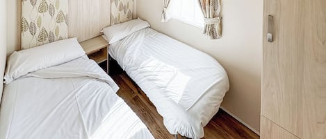 Una habitación con dos camas individuales, un armario de madera y una ventana con cortinas de hojas.