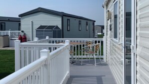A covered outdoor deck with a white railing, a table and chairs, and a building with a garage in the background.