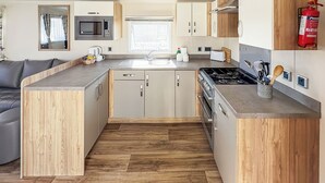 A compact kitchen with wooden cabinetry, a built-in microwave, a stove, and a sink.
