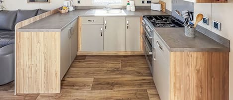 A compact kitchen with wooden cabinetry, a built-in microwave, a stove, and a sink.