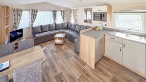 A modern RV interior with a sectional sofa, dining table, kitchen area, and a TV.