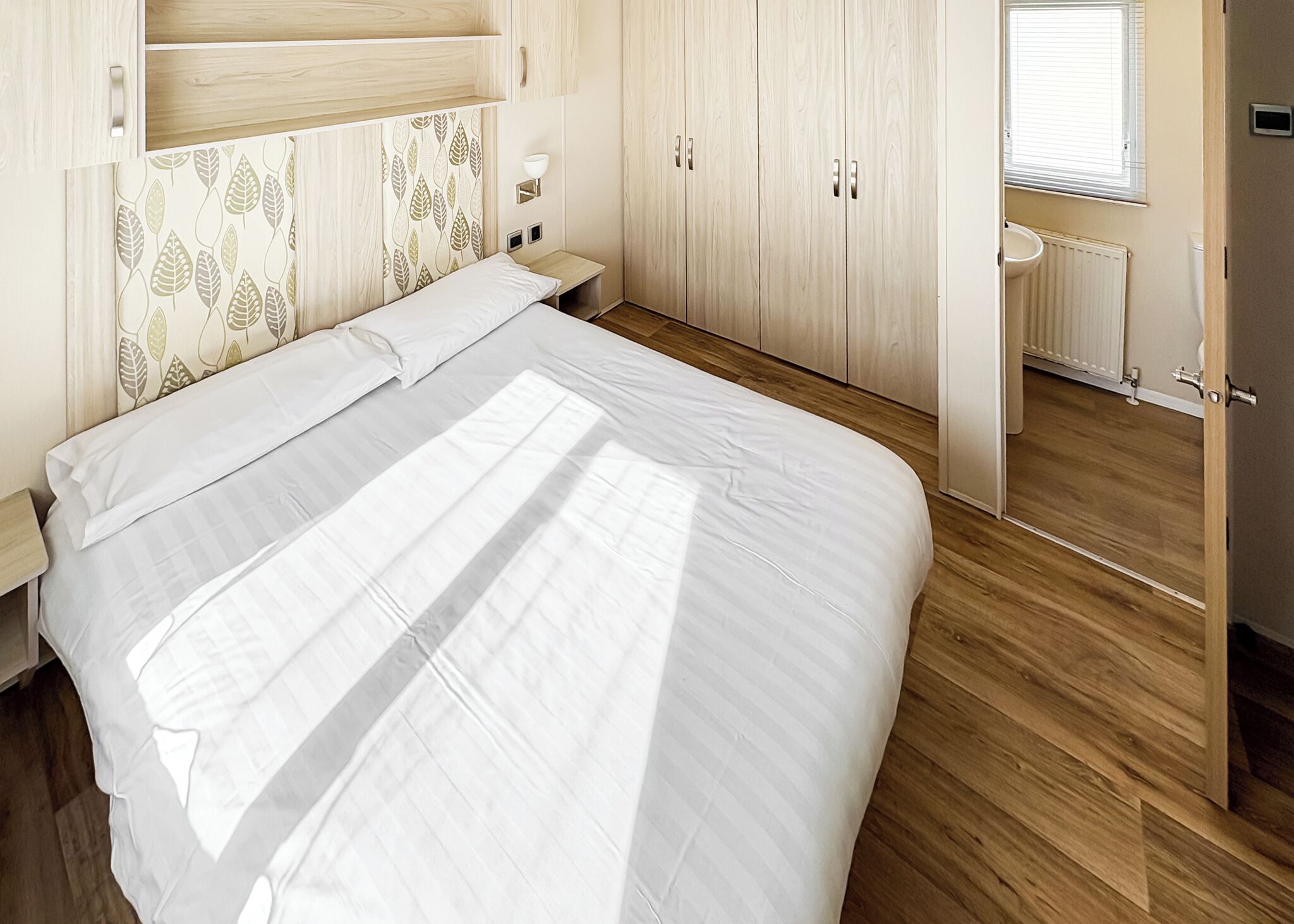 Un dormitorio con cama, armario de madera, mesita de noche y ventana.