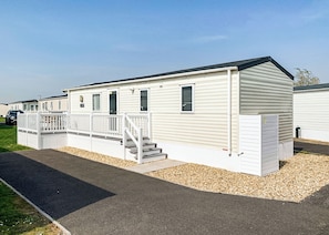 A single-story mobile home with a front porch, a staircase, and a driveway. - Modern and contemporary 12ft-wide caravan with one double and one twin. (Bleadon, Weston-Super-Mare)