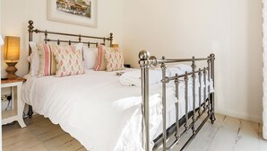 A neatly made bed with a metal frame, a bedside table with a lamp, and a framed picture on the wall.