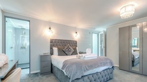 A modern bedroom with a tufted headboard, bedside lamps, a large bed, a mirror, and a walk-in closet. - Chatsworth Superior Pet Friendly (Longnor, Nr. Buxton)
