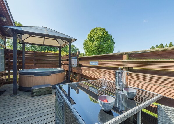 A hot tub under a pergola, a table with glasses and a bowl, and a sign that says "Slippery when wet."