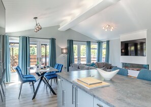 A spacious living area with a large sofa, a dining table with blue chairs, and a kitchen island.