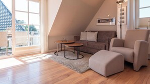 A modern living room with a sofa, armchair, and coffee table, a large window, and a view of the outside.