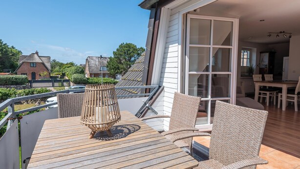 A wooden deck with wicker furniture, a glass door leading to an interior dining area, and a view of neighboring houses.