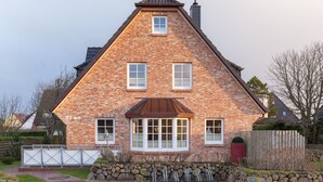 A brick house with a gabled roof, a central bay window, and a stone wall in front.