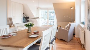 A modern kitchen with white cabinets, a wooden dining table, and a view of the outside through large windows.